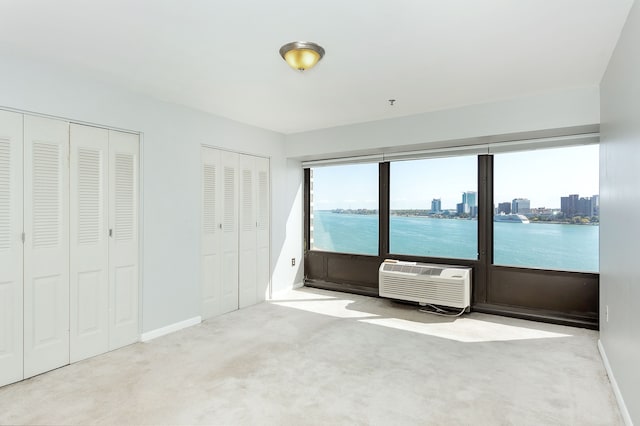 unfurnished bedroom featuring a wall mounted air conditioner, light colored carpet, a water view, and multiple closets