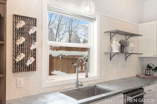 interior details featuring dishwasher, sink, white cabinets, and hanging light fixtures