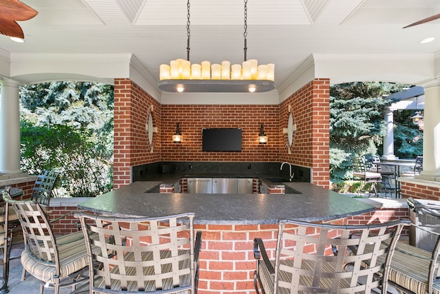 kitchen featuring kitchen peninsula, ornamental molding, brick wall, sink, and pendant lighting