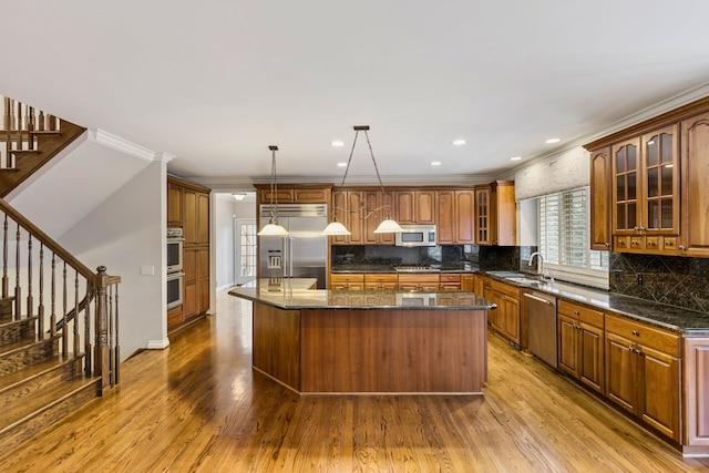 kitchen with crown molding, light hardwood / wood-style floors, pendant lighting, a kitchen island, and appliances with stainless steel finishes