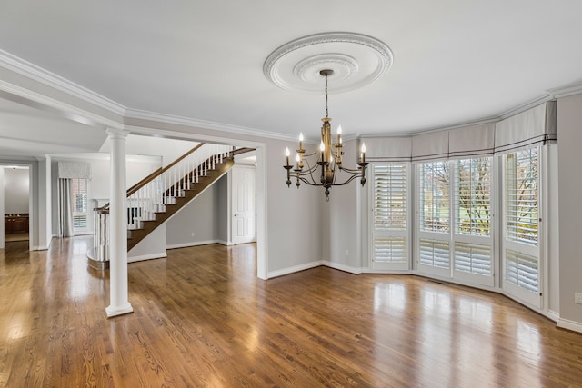 unfurnished dining area featuring ornate columns, hardwood / wood-style flooring, ornamental molding, and a notable chandelier