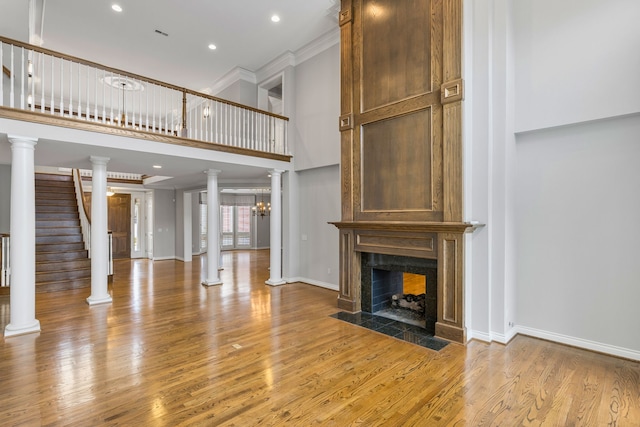 unfurnished living room with ornate columns, a fireplace, light hardwood / wood-style floors, and ornamental molding