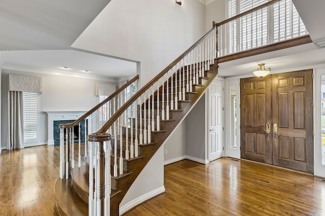 foyer entrance with wood-type flooring, ornamental molding, and a high end fireplace