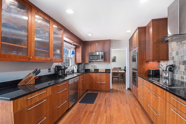 kitchen featuring light hardwood / wood-style floors, sink, appliances with stainless steel finishes, wall chimney exhaust hood, and dark stone counters