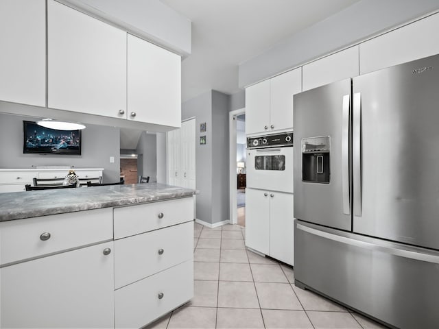 kitchen with white cabinets, stainless steel fridge, oven, and light tile patterned flooring