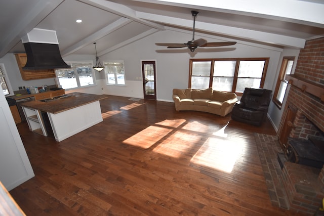 living room with ceiling fan, dark wood-type flooring, a brick fireplace, and vaulted ceiling with beams