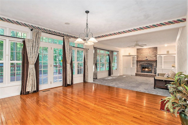 unfurnished living room featuring ceiling fan with notable chandelier, light wood-type flooring, a textured ceiling, and a brick fireplace