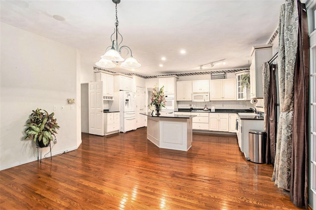 kitchen featuring white appliances, white cabinets, a center island, dark hardwood / wood-style floors, and hanging light fixtures