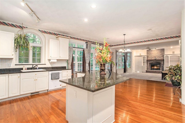 kitchen with sink, a brick fireplace, white dishwasher, decorative light fixtures, and white cabinets