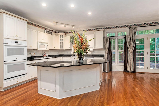 kitchen featuring tasteful backsplash, white appliances, dark stone countertops, white cabinets, and a kitchen island