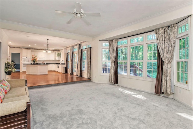 unfurnished living room featuring ceiling fan with notable chandelier, light colored carpet, and ornamental molding