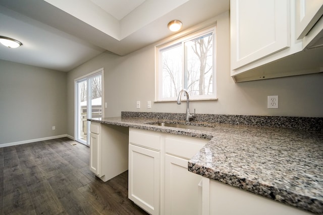 kitchen with light stone countertops, dark hardwood / wood-style flooring, white cabinets, and sink