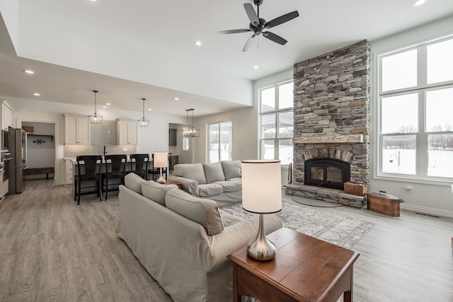 living room with light hardwood / wood-style flooring, a stone fireplace, and ceiling fan