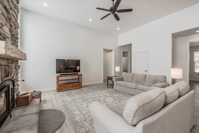 living room featuring a stone fireplace, ceiling fan, light hardwood / wood-style flooring, and a high ceiling