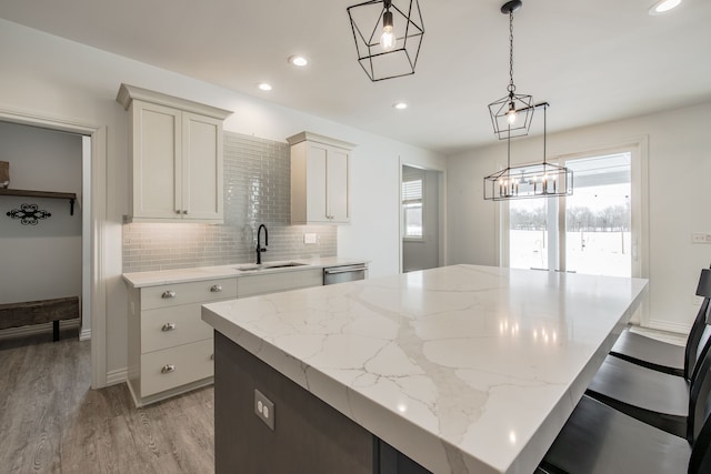 kitchen featuring a center island, sink, hanging light fixtures, light stone countertops, and light hardwood / wood-style floors