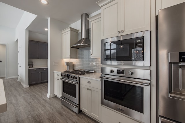 kitchen with light hardwood / wood-style flooring, wall chimney exhaust hood, decorative backsplash, white cabinetry, and stainless steel appliances