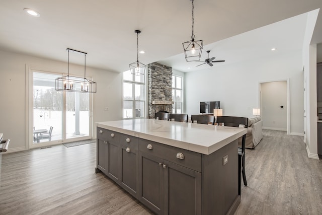 kitchen featuring ceiling fan, a stone fireplace, decorative light fixtures, a breakfast bar area, and a kitchen island