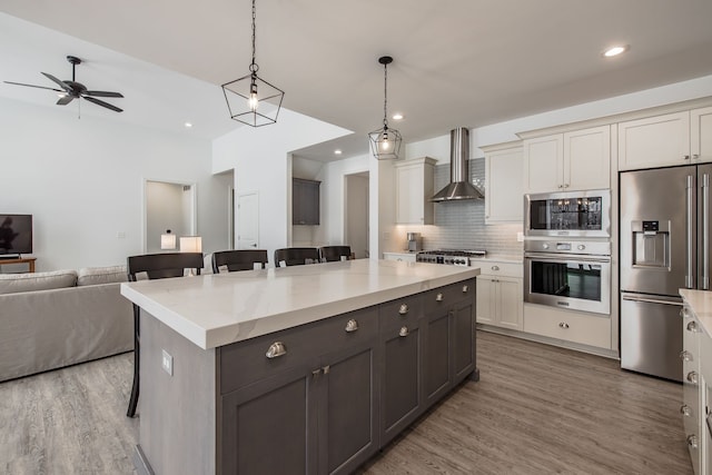 kitchen featuring a kitchen bar, backsplash, wall chimney exhaust hood, stainless steel appliances, and hanging light fixtures