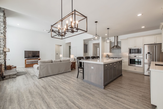 kitchen featuring wall chimney exhaust hood, hanging light fixtures, backsplash, a kitchen island, and appliances with stainless steel finishes