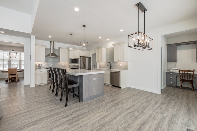 kitchen featuring wall chimney range hood, hanging light fixtures, a breakfast bar area, a kitchen island, and stainless steel appliances