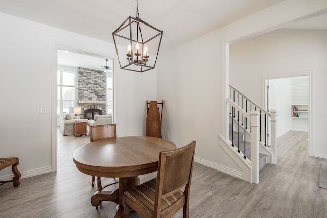 dining area featuring a stone fireplace, ceiling fan with notable chandelier, and light wood-type flooring