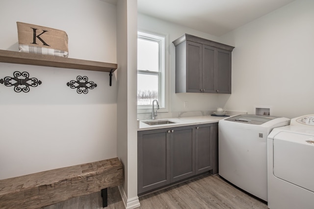 laundry area featuring washing machine and clothes dryer, sink, cabinets, and light wood-type flooring