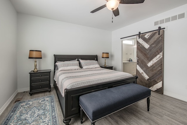 bedroom featuring connected bathroom, a barn door, ceiling fan, and wood-type flooring