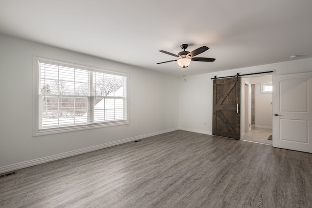 unfurnished bedroom featuring ceiling fan, a barn door, and wood-type flooring