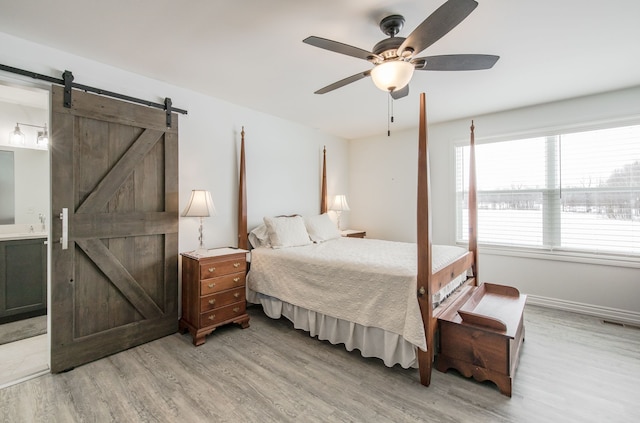 bedroom featuring a barn door, ceiling fan, ensuite bathroom, and light hardwood / wood-style floors