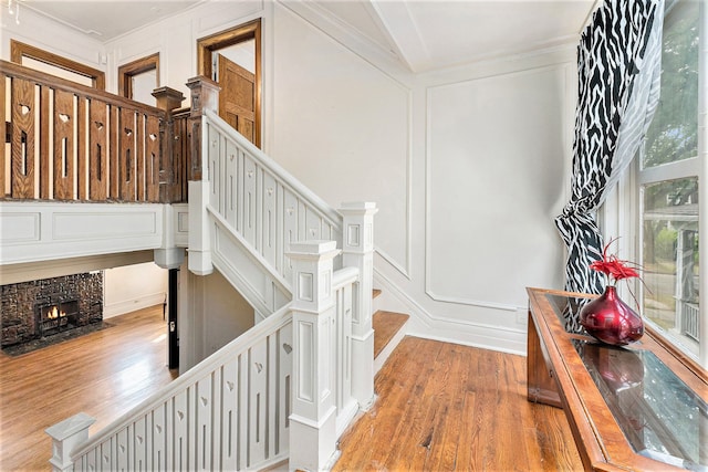 stairway featuring hardwood / wood-style flooring, a stone fireplace, and ornamental molding