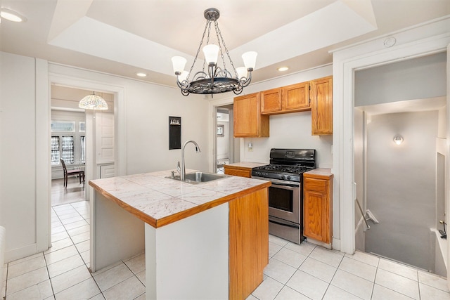 kitchen featuring gas range, a raised ceiling, sink, decorative light fixtures, and an island with sink