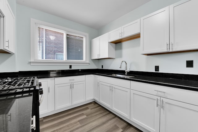 kitchen featuring white cabinetry, sink, black range oven, dark stone counters, and light hardwood / wood-style floors