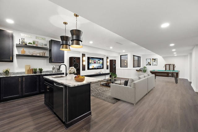 interior space featuring sink, light stone counters, dark hardwood / wood-style flooring, decorative light fixtures, and a kitchen island with sink