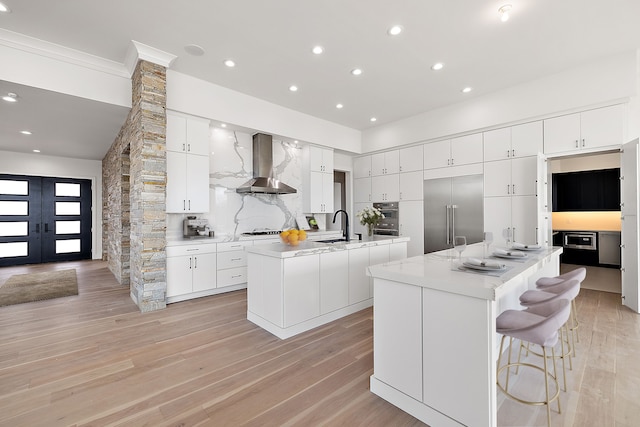 kitchen with white cabinets, built in appliances, a spacious island, and wall chimney range hood