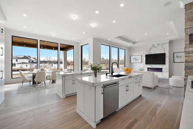 kitchen with sink, stainless steel dishwasher, an island with sink, a fireplace, and white cabinets