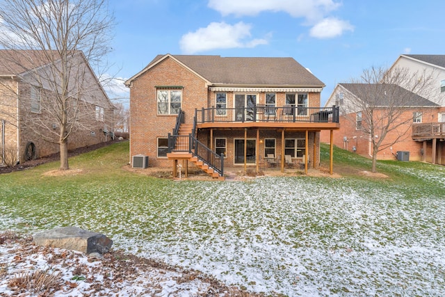 snow covered back of property with a wooden deck, a yard, and central AC