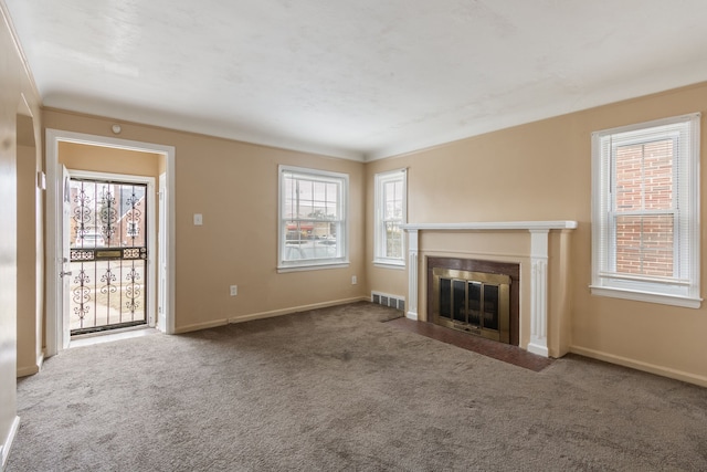 unfurnished living room featuring a healthy amount of sunlight, crown molding, and carpet floors