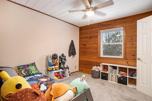 recreation room with carpet flooring, ceiling fan, ornamental molding, and wood walls