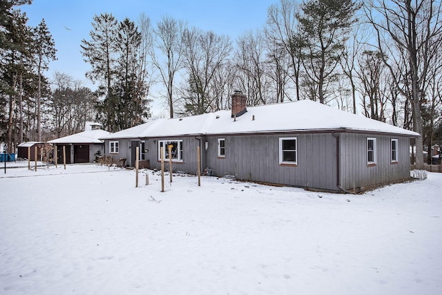 snow covered back of property featuring an outdoor structure