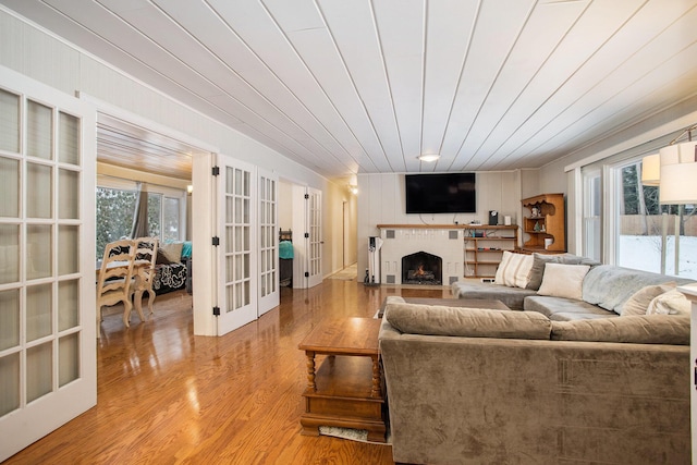 living room with a fireplace, wood ceiling, french doors, and light hardwood / wood-style flooring