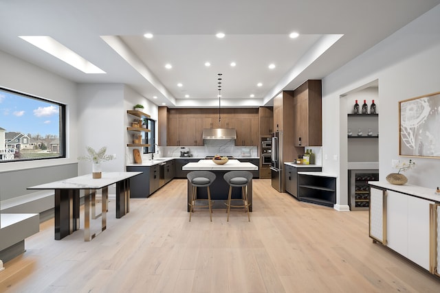 kitchen featuring a raised ceiling, light hardwood / wood-style floors, a kitchen bar, dark brown cabinets, and a kitchen island