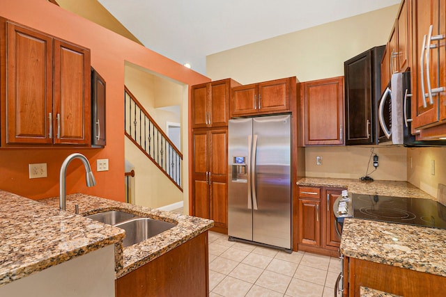 kitchen featuring light tile patterned floors, brown cabinetry, light stone countertops, stainless steel appliances, and a sink