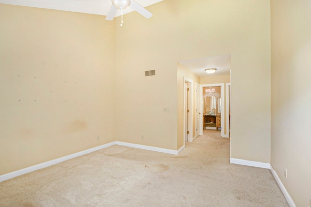 unfurnished room with visible vents, a high ceiling, light carpet, ceiling fan, and baseboards