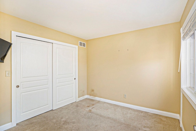 unfurnished bedroom with light carpet, baseboards, visible vents, and a closet