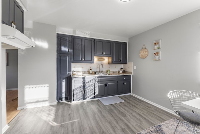 bar featuring decorative backsplash, sink, light stone countertops, and light hardwood / wood-style flooring