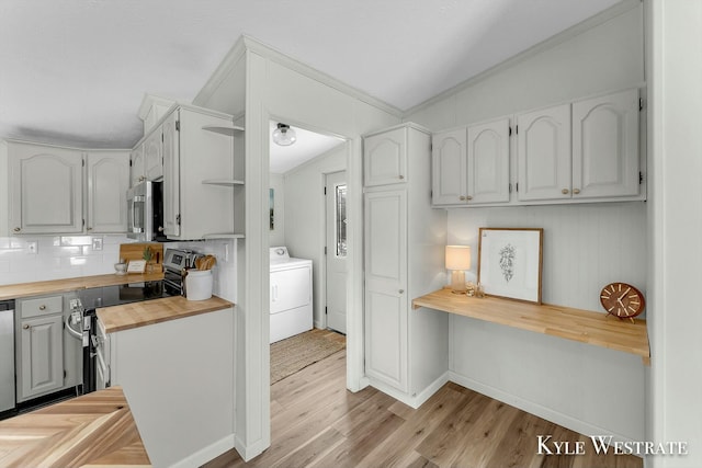 kitchen with stainless steel appliances, vaulted ceiling, washer / dryer, butcher block countertops, and white cabinetry