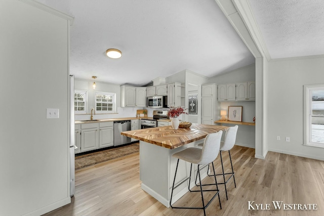 kitchen with appliances with stainless steel finishes, a breakfast bar, sink, light hardwood / wood-style floors, and butcher block counters