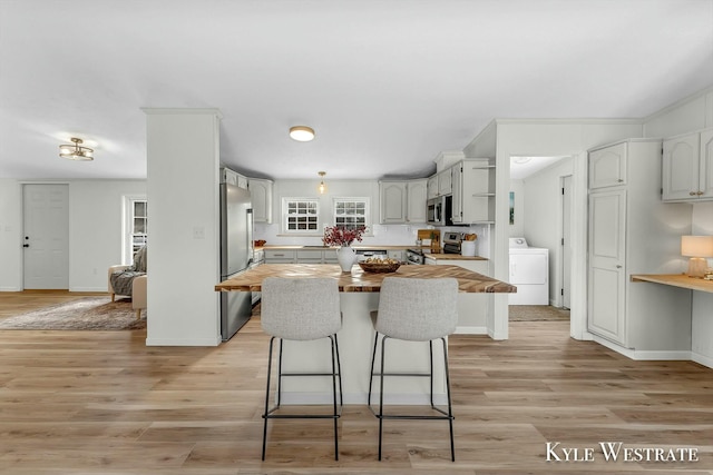 kitchen featuring light wood-type flooring, stainless steel appliances, white cabinets, washer / clothes dryer, and butcher block counters