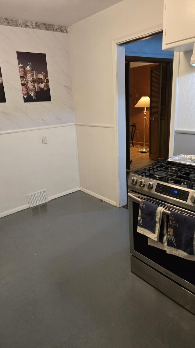 kitchen featuring stainless steel gas stove, concrete floors, visible vents, and white cabinets