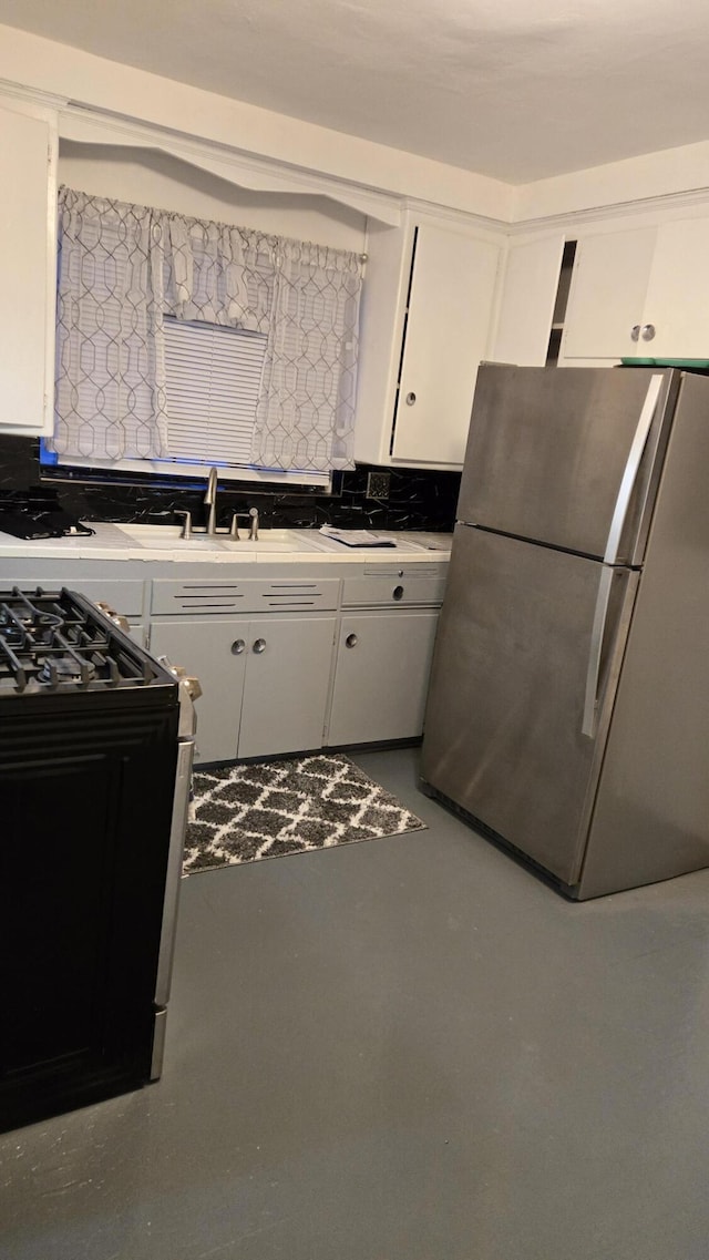 kitchen featuring freestanding refrigerator, gas range oven, light countertops, concrete flooring, and white cabinetry